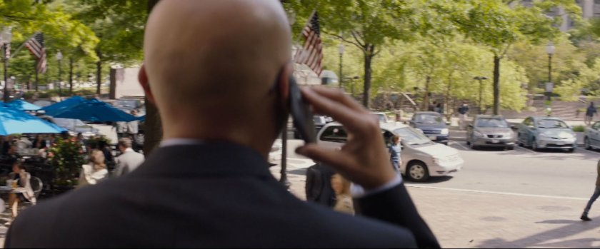 Agent Sitwell on the phone looking across a street towards a park.