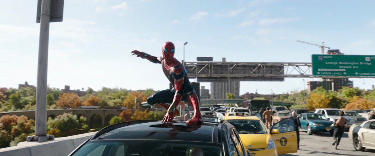 Spider-Man perches on top a car parked on a freeway bridge.