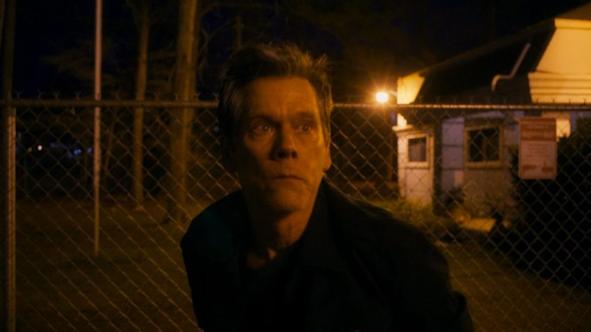 Kevin Bacon in front of a fence.